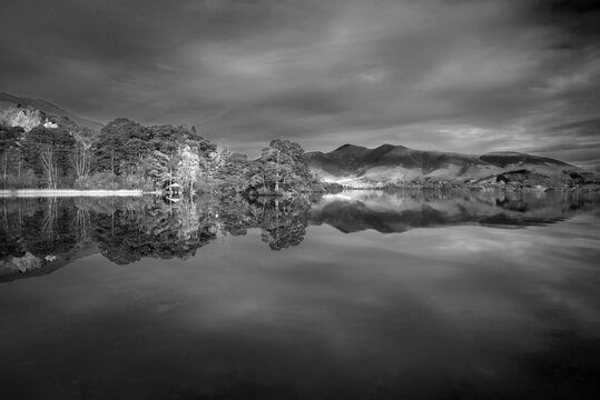 Black and white Absolutely stunning vibrant Autumn sunrise landscape image looking from Manesty Park in Lake Distict towards sunlit Skiddaw Range with mit rolling across Derwentwater surface