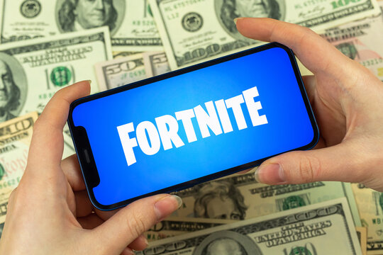 Person uses Apple iPhone for playing Fortnite game. Logo close-up, money, dollar bills business background photo