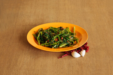 Sambal Kang Kong vegetable with raw garlic and chili pepper in plate on wooden table top view Chinese food