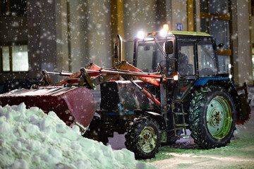 Snowplow truck, tractor  removing snow on the road street in blizzard snowstorm at night. Snow...