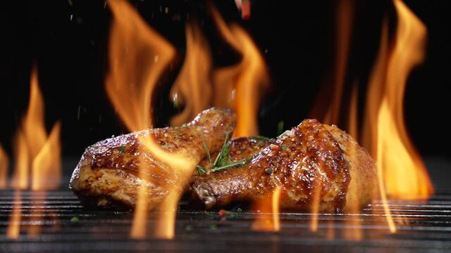Chicken drumsticks or legs grilled on hot barbecue charcoal flaming grill with spices sprinkled on top. Juicy chicken meat roasted on bbq grill. slow motion