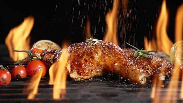 Chicken thighs grilled on hot barbecue charcoal flaming grill with spices sprinkled on top. Juicy chicken meat roasted on bbq grill. slow motion