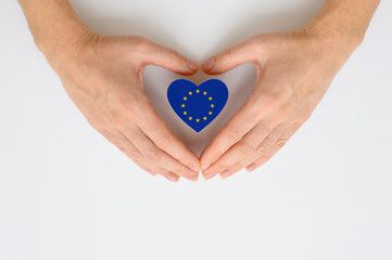 EU flag in the shape of a heart in female hands on a light background.