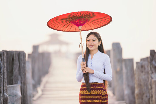 A young Burmese woman is walking with a red umbrella on U-bein bridge, Mandalay, Myanmar.