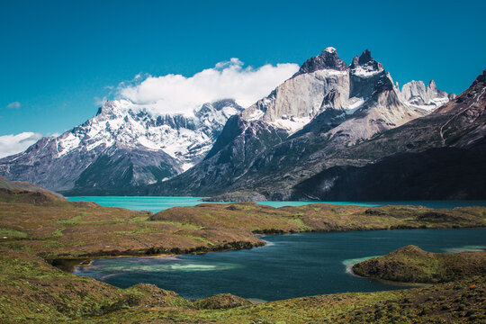 Snowy mountains with clouds on top with lakes in front in the Torres del Paine area of ​​Chilean Patagonia
