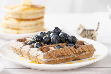 Belgian waffles with fruits berries and honey maple syrup set on white cafe table.
