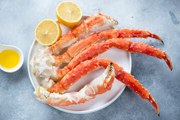 White plate with boiled claws of kamchatka crab, lemon and butter over light-blue stone background, studio shot