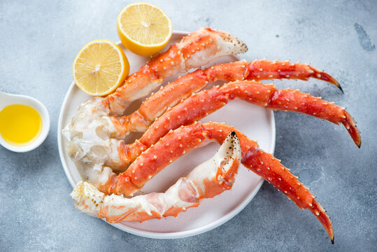 White plate with boiled claws of kamchatka crab, lemon and butter over light-blue stone background, studio shot
