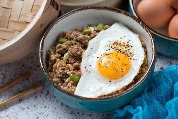 Ground meat and fried rice topped with a fried egg and served in a turquoise bowl, middle close-up, studio shot