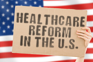 The phrase " Healthcare reform in the U.S. " on a banner in men's hand with blurred American flag on the background. Nation. Crisis. Problem. Medical help. Reformation. Clinical