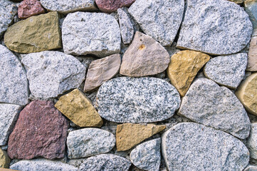 Background of stones. A wall of multicolored stones. The masonry is made of untreated stones. A wall of large stones.