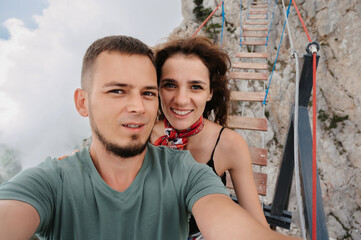 Fototapeta na wymiar Selfie-portrait of a young couple in love against the backdrop of a mountainous area and a rope bridge. The concept of tourism, shared recreation