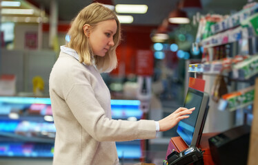 Woman pays at self-checkouts in supermarket. - obrazy, fototapety, plakaty