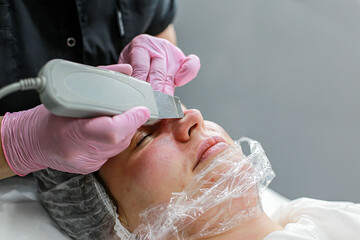 Cosmetologist girl does ultrasonic cleaning of the face