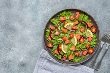 Fresh salad with salmon, tomato, lettuce leaves, microgreens, red onion and sesame seeds. Gray concrete rustic background. Top view, flat lay.