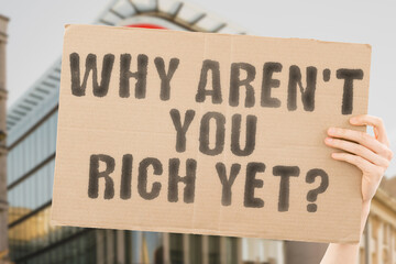 The question " Why aren't you rich yet? " on a banner in men's hand with blurred background. Planning. Payment. Save. Win. Entrepreneurship. Work. Persistence. Million. Accumulate