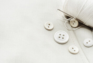 Needle with white threads, buttons on white fabric, clothes. Part of men's clothing.