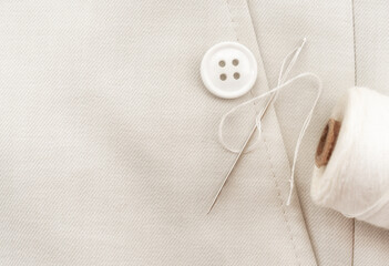 Needle with white threads, buttons on white fabric, clothes. Part of men's clothing.