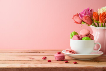 Fototapeta na wymiar Macaroons french cookies on wooden table with rose flower bouquet on wooden table over pink background. Valentines day or Mothers day concept