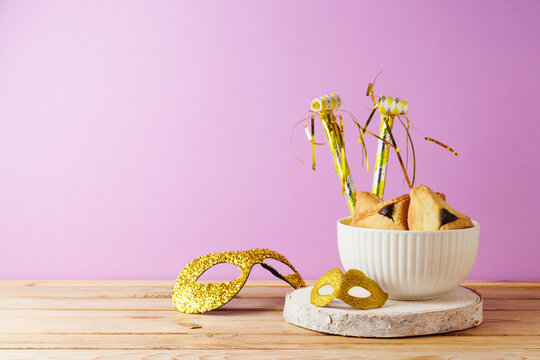Hamantaschen cookies  and carnival mask on wooden table over violet purple background for jewish holiday Purim.