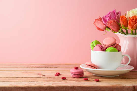 Macaroons french cookies on wooden table with rose flower bouquet on wooden table over pink background. Valentines day or Mothers day concept