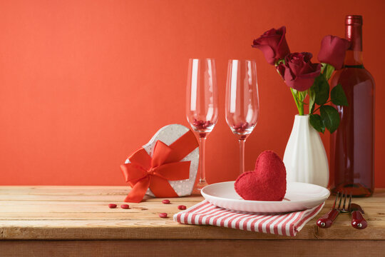 Valentines day romantic dinner concept. Wooden table with plate, wine bottle and rose flowers over red background