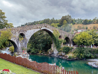 Vistas del paisaje del Puente romano de Covadonga con el río de aguas turquesas y cielo nuboso con una montaña verde al fondo en Cangas de Onís, Asturias, verano de 2020