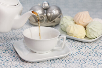 Hostess pours tea into cups from the kettle, in a piece with delicious fresh marshmallows, on festive table