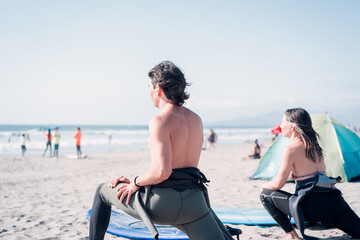 two latin surfers stretching before getting into the water to surf the waves in La Serena, back view