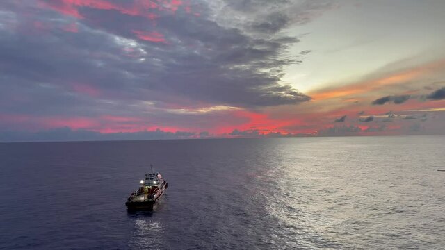 Supply vessel or crew boat with offshore oil and gas production platform in sun rise time with buetiful orange clouds and reflect of sun beam on the sea.