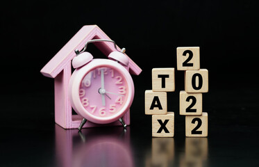 Tax Concept. Tax 2022 word is written on wood block and clock on black background.                           