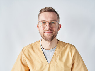 Obraz premium Close up portrait of a male doctor or nurse with his arms raising up eyeglasses. Portrait of a handsome caucasian male doctor wearing eyeglasses and beige medical uniform. High quality photo