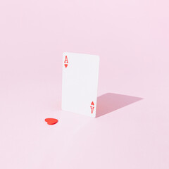 Playing card ace of hearts on pink pastel background with a lonely heart separated from the middle. Flat lay minimal concept. Valentines day inspiration. Layout design. Gambling mood.