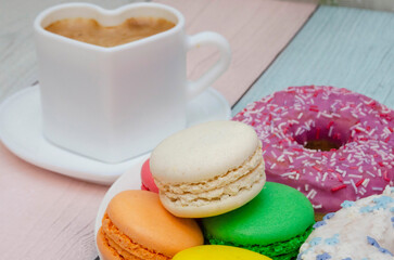 Obraz na płótnie Canvas Delicious fragrant coffee in a heart-shaped mug with colorful sweet macaroons