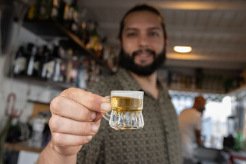 Bartender shows a tiny jarr of beer in a beach bar