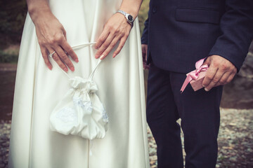 Close-up of bride holding white wedding bag and groom holding a gift box.