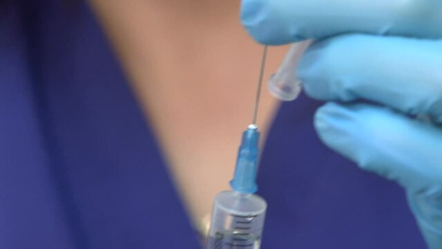 Doctor in latex gloves fill in syringe with medicine from glass vial, close up. Health doctor nurse pulling Covid-19 vaccine liquid from vial
