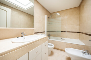 Conventional toilet with cream colored marble walls, recessed mirror and white sink