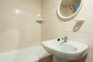 Spartan toilet with small circular mirror, earthenware sink and enamel bathtub