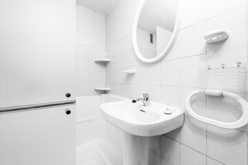 Toilet with white cabinet, ceramic sink, towel rails and white circular mirror with white tiles