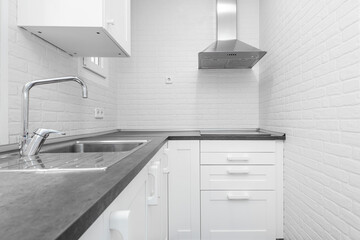 Vacation rental kitchen with white cabinets, white brick walls, gray countertop and stainless steel sink and range hood in the corner