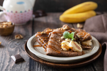 Celebrating Pancake day, healthy breakfast. Delicious homemade chocolate crepes with nuts, caramel, bananas on rustic wooden table.
