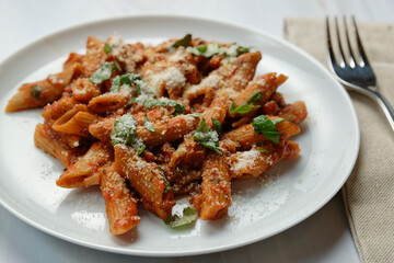 Penne pasta with tomato sauce and basil and parmesan cheese. Served on a plate.