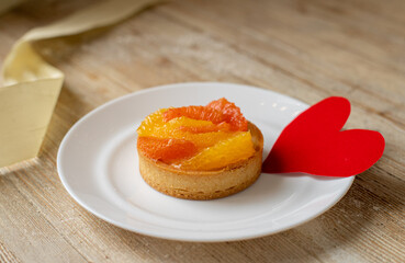 Tartlet - a dessert with tangerine and grapefruit lies on the table with a postcard for Valentine's Day