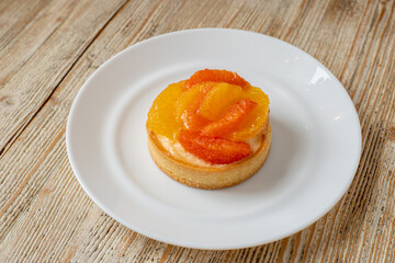 Tartlet with tangerine and grapefruit lies on a plate on a wooden table. beautiful dessert