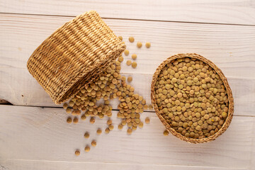 Uncooked organic green lentils with a straw basket on a wooden table, macro, top view.