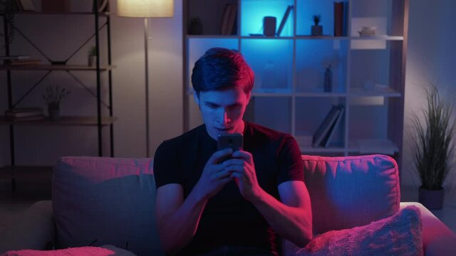 Fast message. Worried man. Meme expression. Worried guy typing on smartphone sitting sofa in dark neon light room interior looped video.