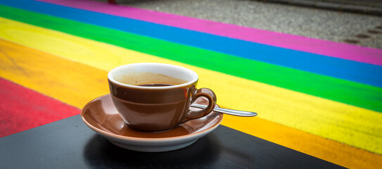 One cup of coffee on a table in a rainbow street. Equal rights for LGBTQ+ community street art....