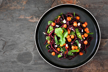 Healthy beet noodles topped with spinach and chickpeas. Top view on a dark slate background.
