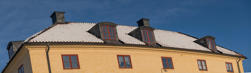 Snowy roof with chimneys and dormers on a 1700s yellow house on the island Drottningholm a sunny day in Stockholm